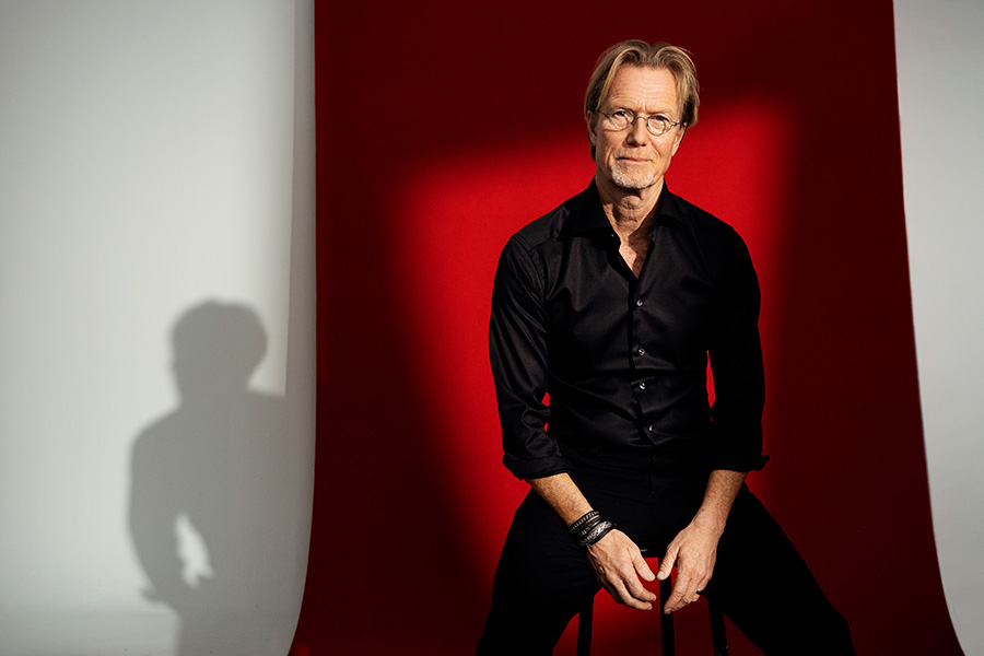 Författaren Anders Roslund sitter på en stol med röd bakgrund.